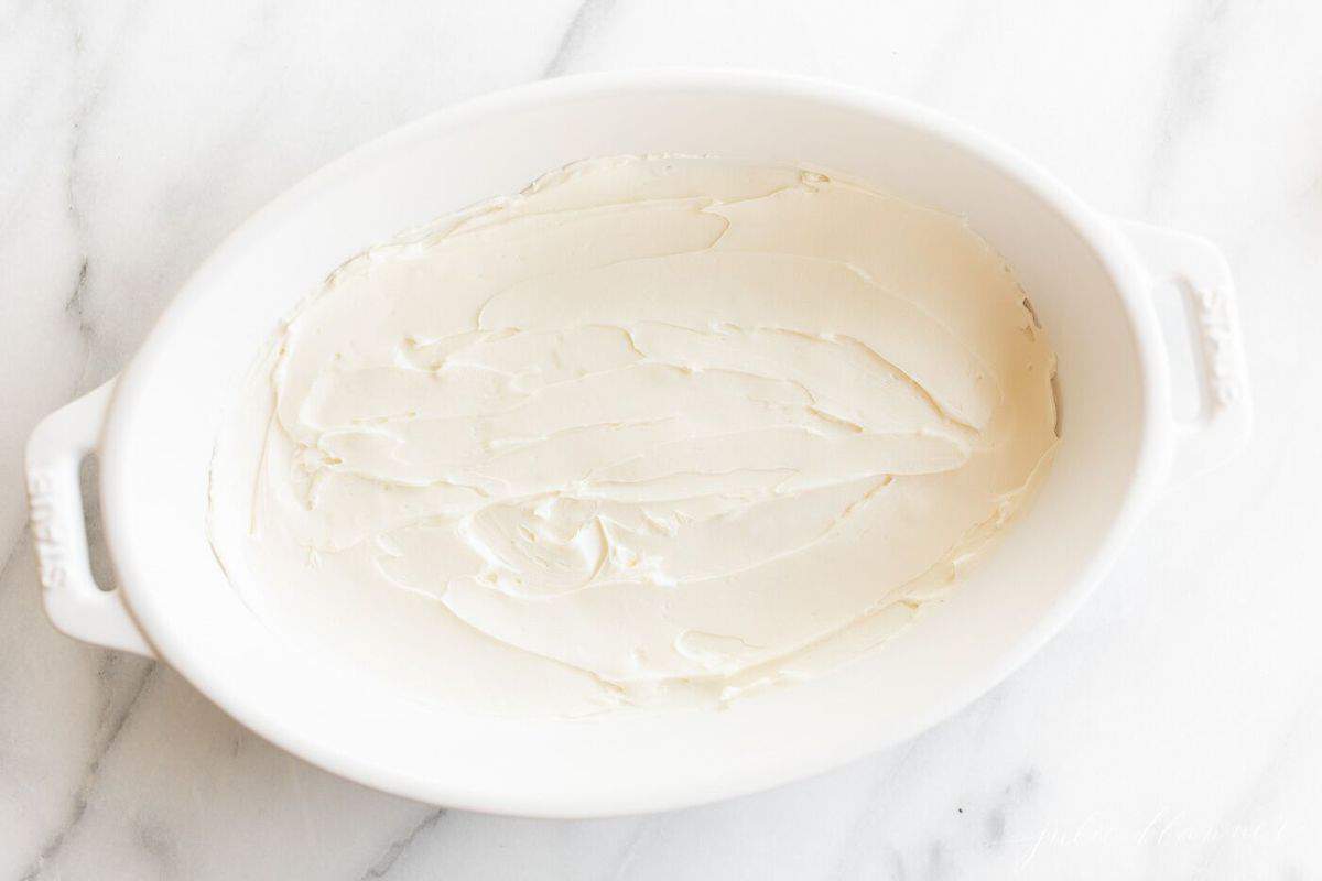 White oval baking dish with cream cheese inside on a kitchen counter.