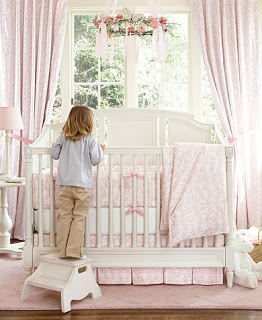A little girl standing on a stool to look inside a crib. 