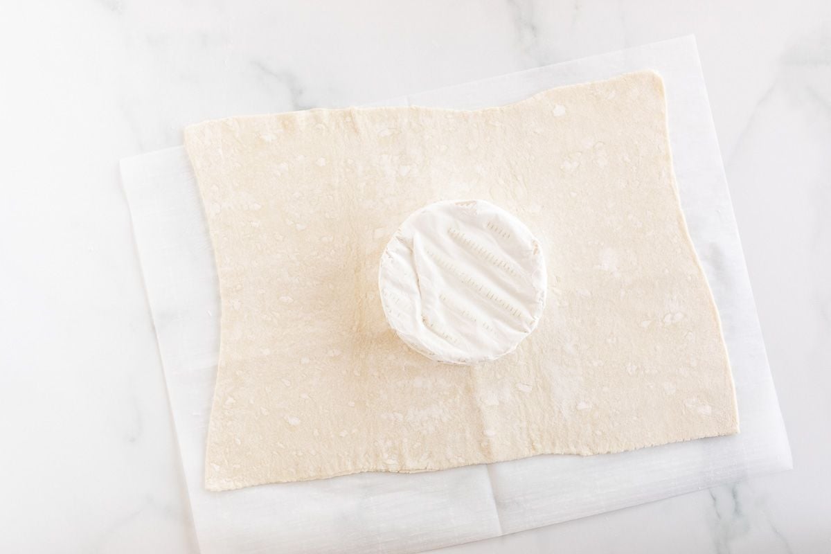 A sheet of puff pastry under a round of brie.