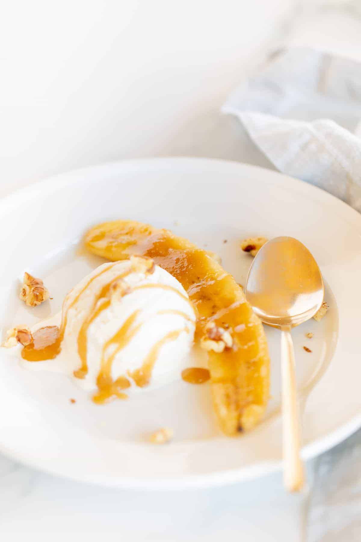 A serving of bananas foster on a white plate, drizzled with caramel sauce and nuts.