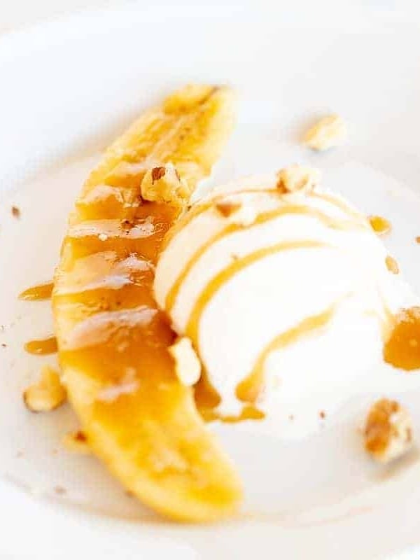 A serving of bananas foster on a white plate, drizzled with caramel sauce and nuts.