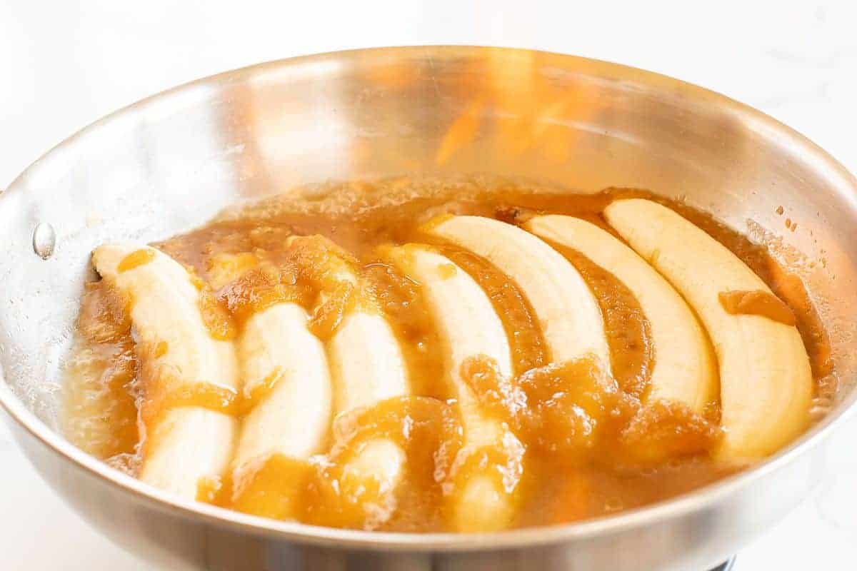 Bananas flambe in a silver saute pan surrounded by caramel sauce.