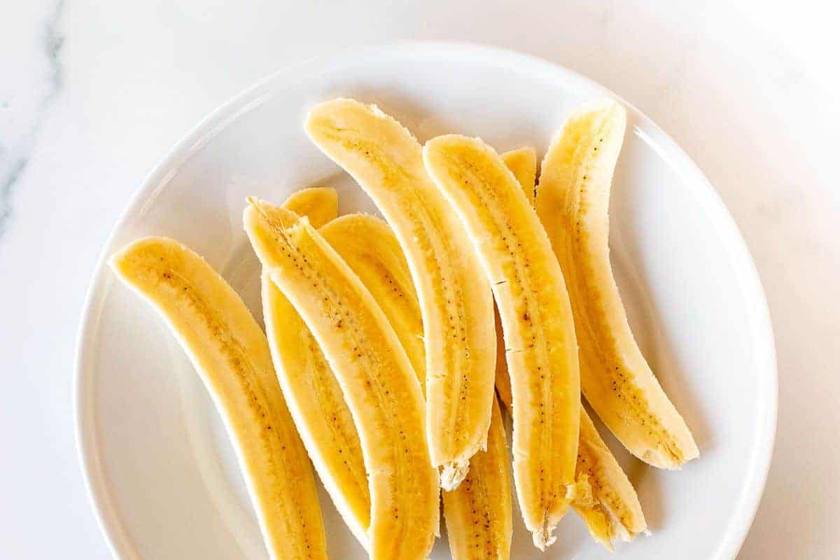 Bananas, sliced in half on a white plate.