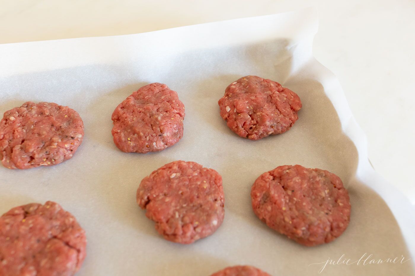 Raw beef, sliders getting ready to go into oven on parchment paper.