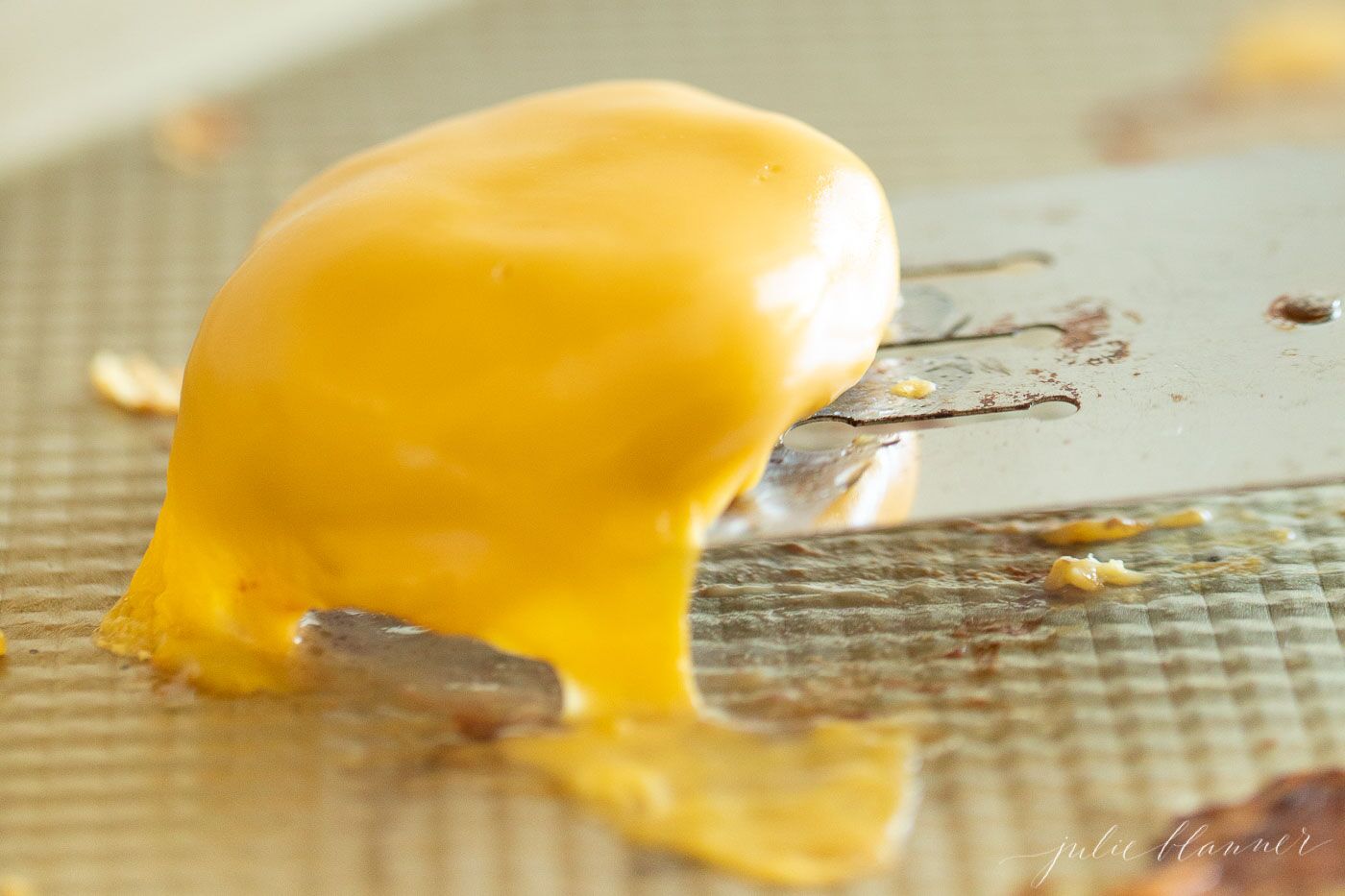 Mini slider burger being lifted off the pan, covered in melting cheese.