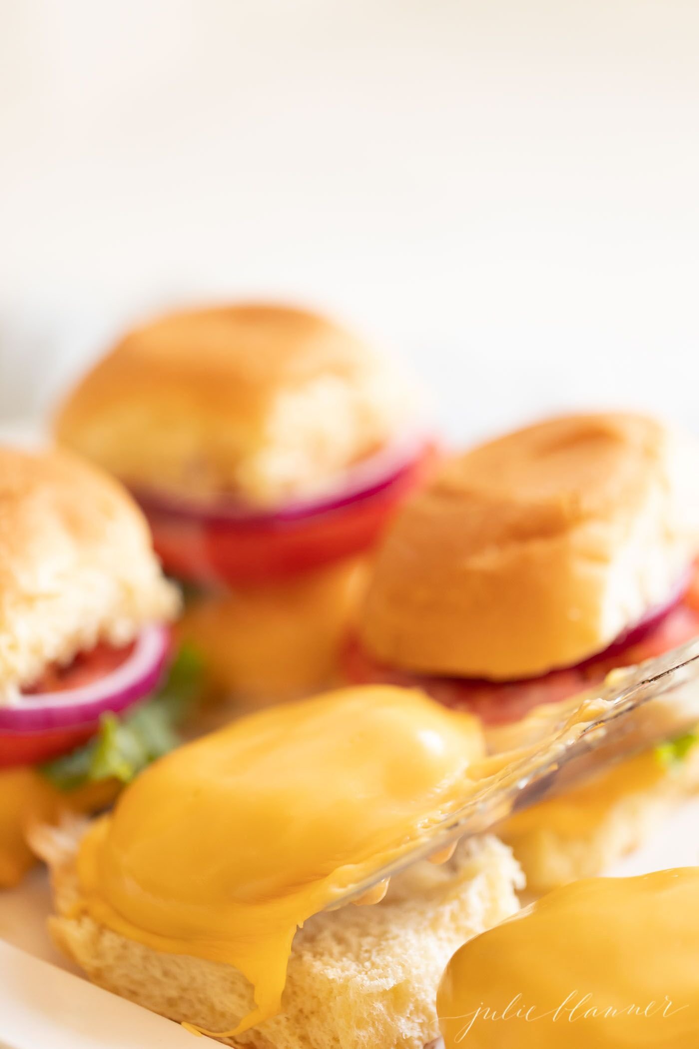 A group of 4 sliders, with patty covered in cheese in the foreground. #sliders.