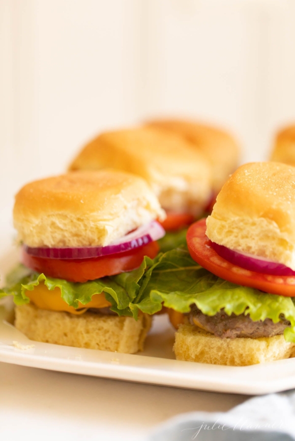 Platter with mini sliders, stacked with onion lettuce and tomato. #sliders