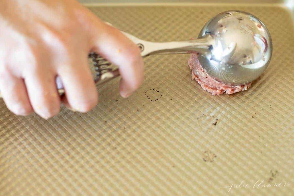 Burgers being made on a baking sheet, which are being scooped with an ice cream scooper.