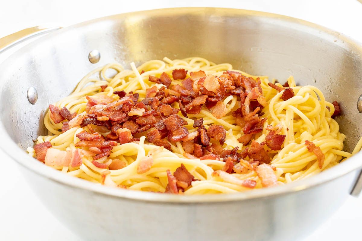 A silver pot full of cooked spaghetti topped with crumbled bacon