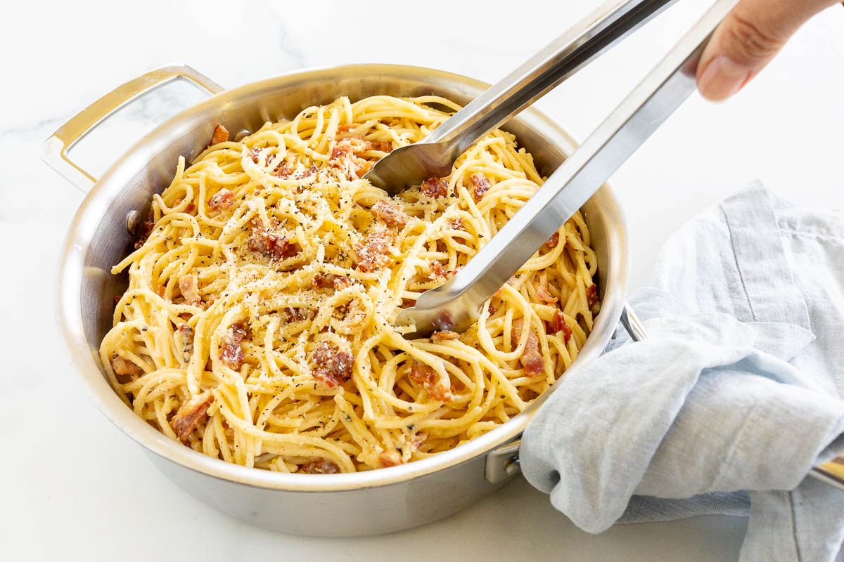 A large silver pot filled with spaghetti in carbonara sauce