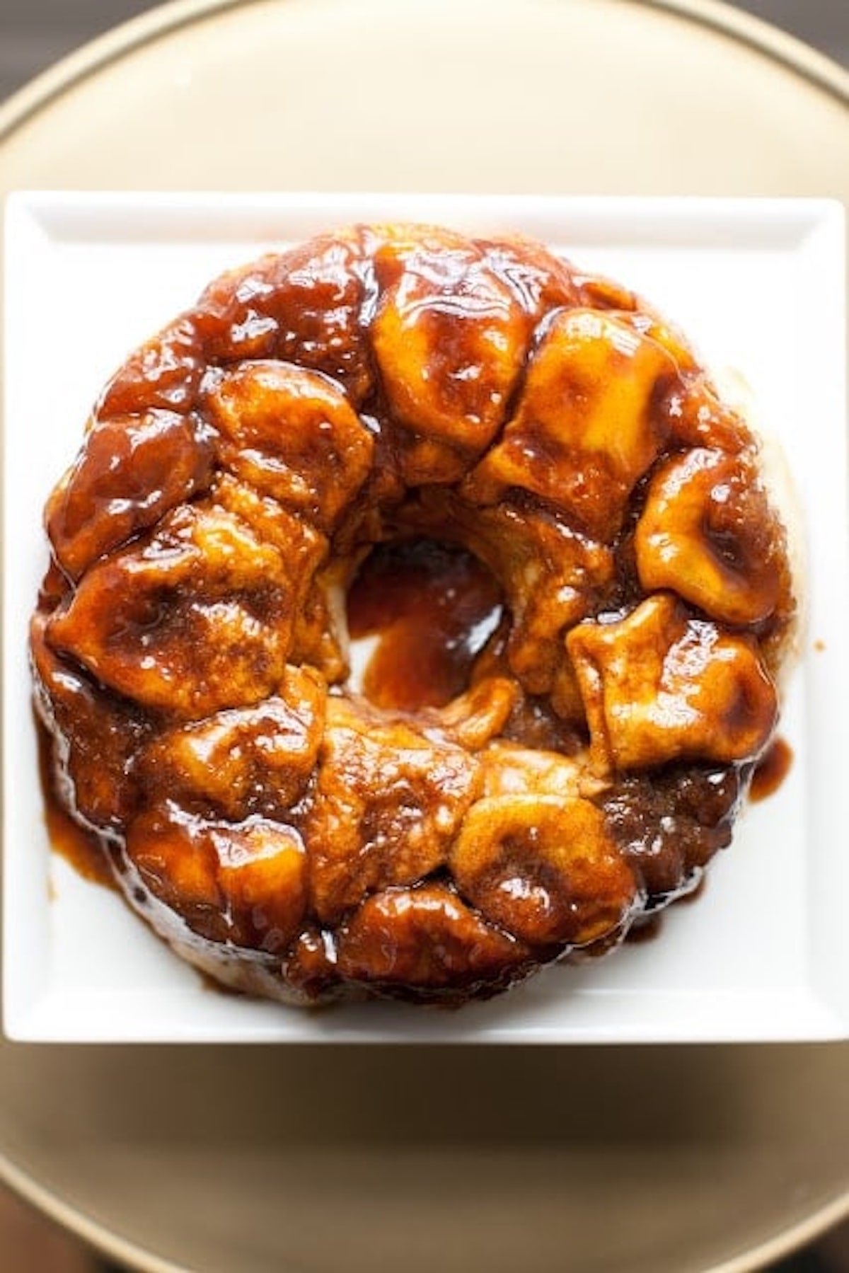 Close-up of a round sticky overnight monkey bread on a white plate, showing pieces of baked dough coated in caramelized sugar.