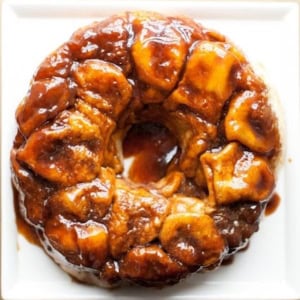 An overhead view of monkey bread dessert, featuring pieces of dough baked together and coated in a caramelized sauce, on a white plate.