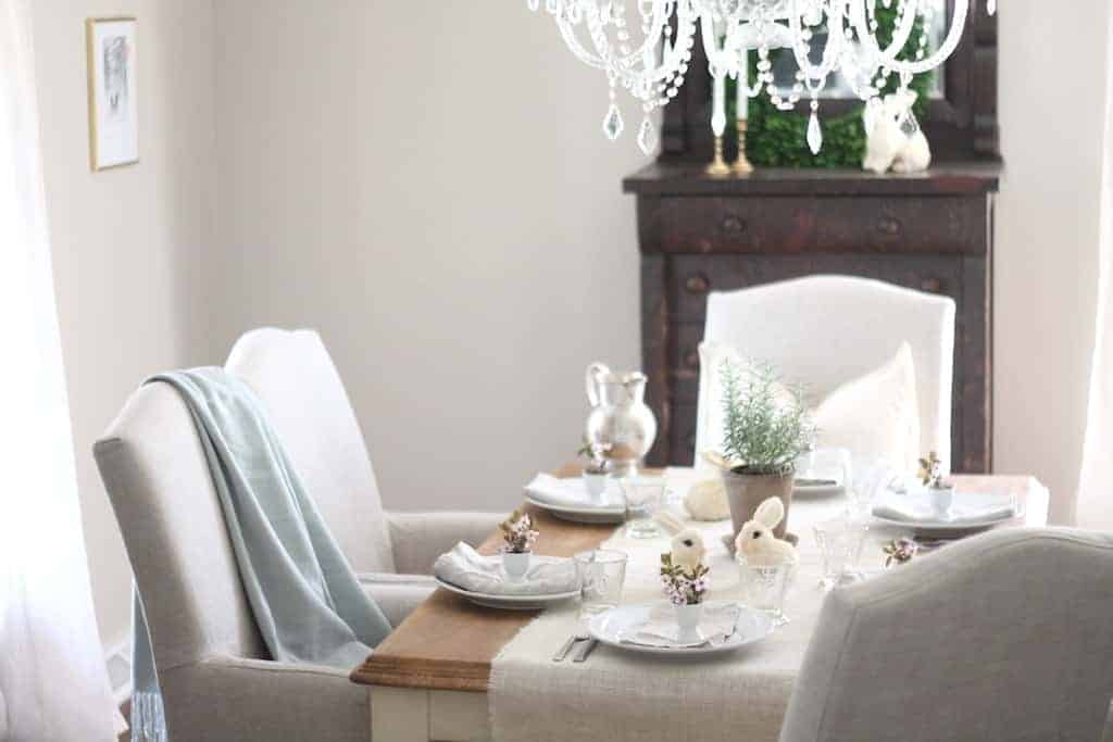 An Easter table setting featuring a burlap runner, pretty glassware and white plates.