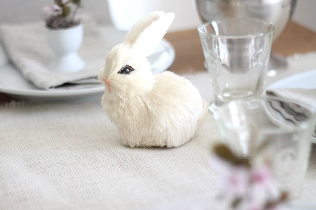 A small textured Easter bunny on a spring table setting, placed on top of a burlap tablecloth.
