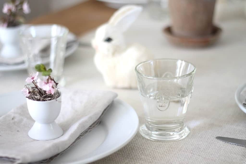 An Easter table setting featuring a burlap runner, pretty glassware and white plates.