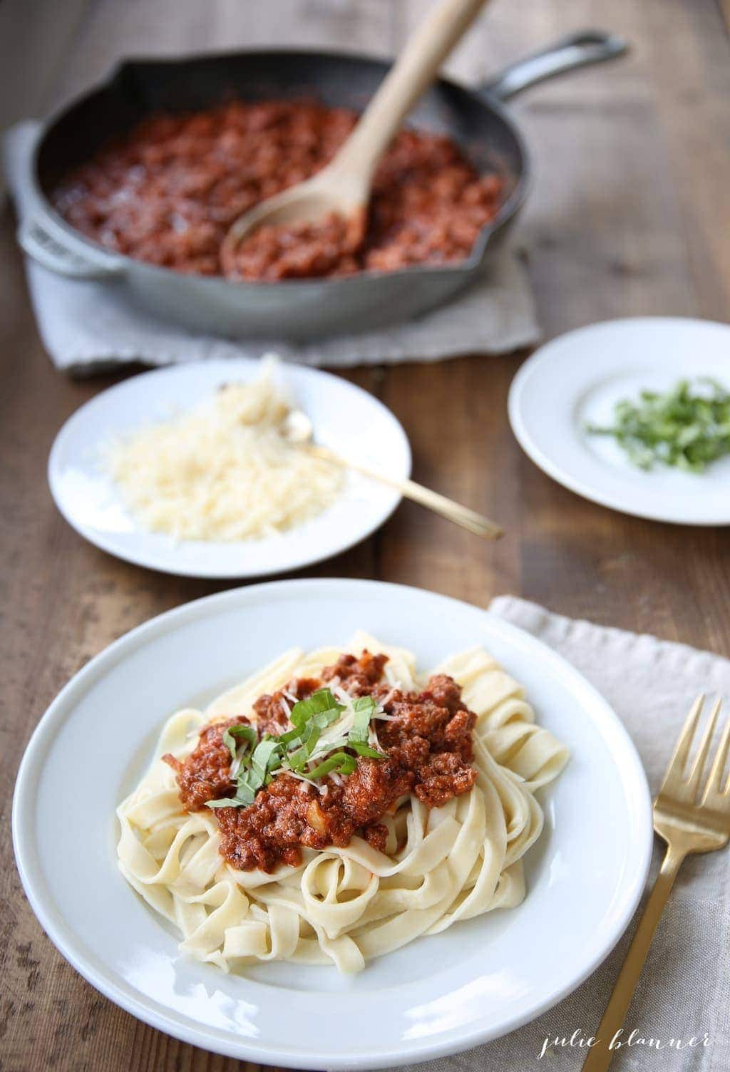 pasta bolognese on white plate by saucepan with sauce and plate of cheese