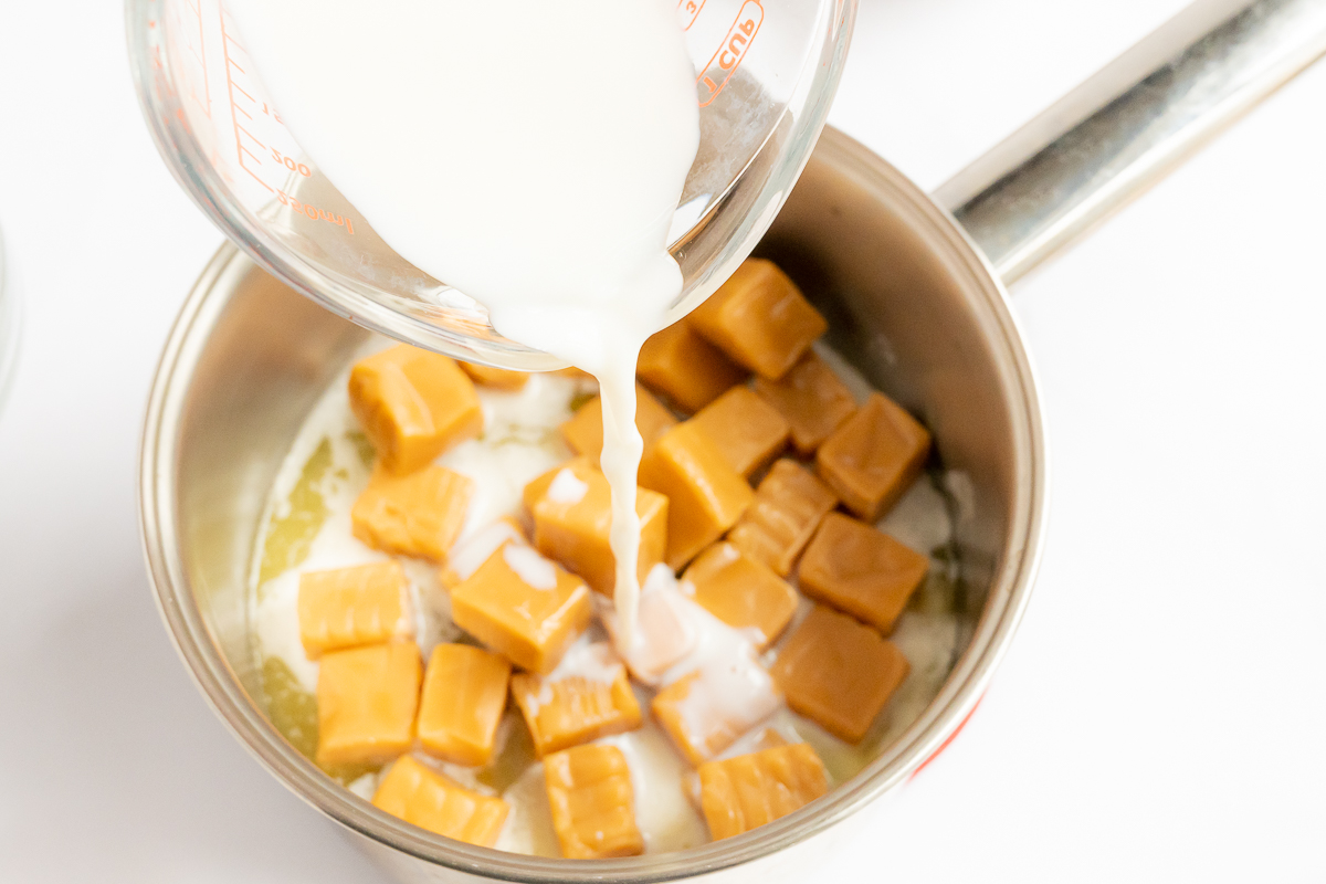 Caramel cubes being poured into a pan with milk for a delicious caramel pecan pie recipe.