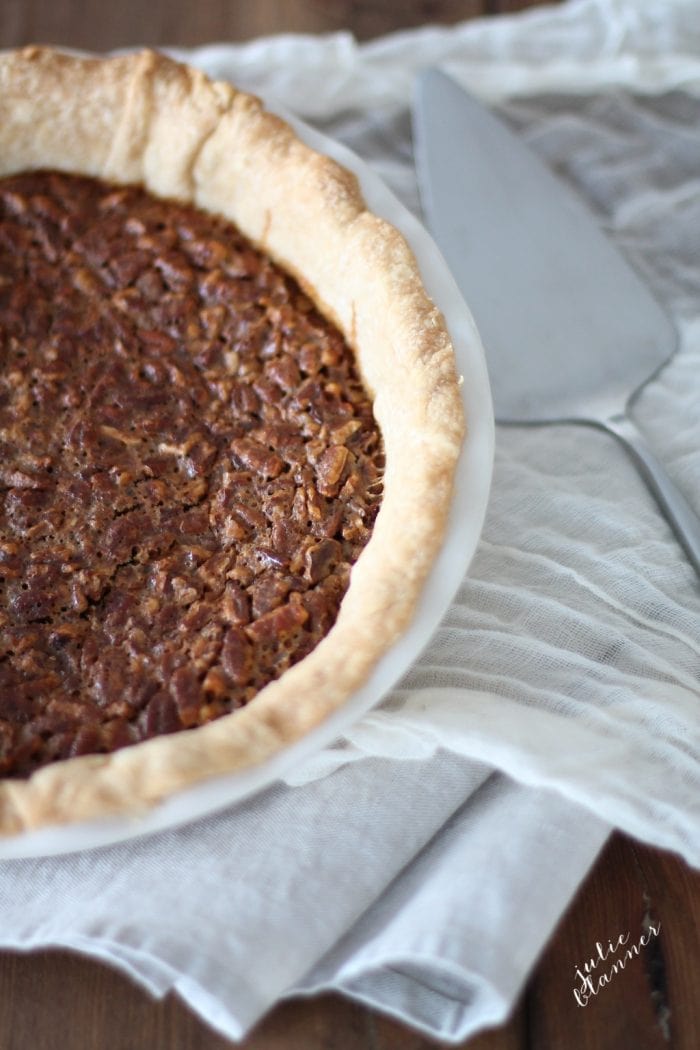 Caramel pecan pie in a white pie pan, a pie cutter to the side. 