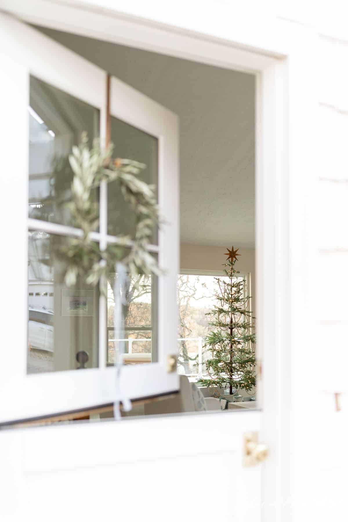 A dutch door with a DIY wreath hanging on the windows, looking into a living room decorated for Christmas.