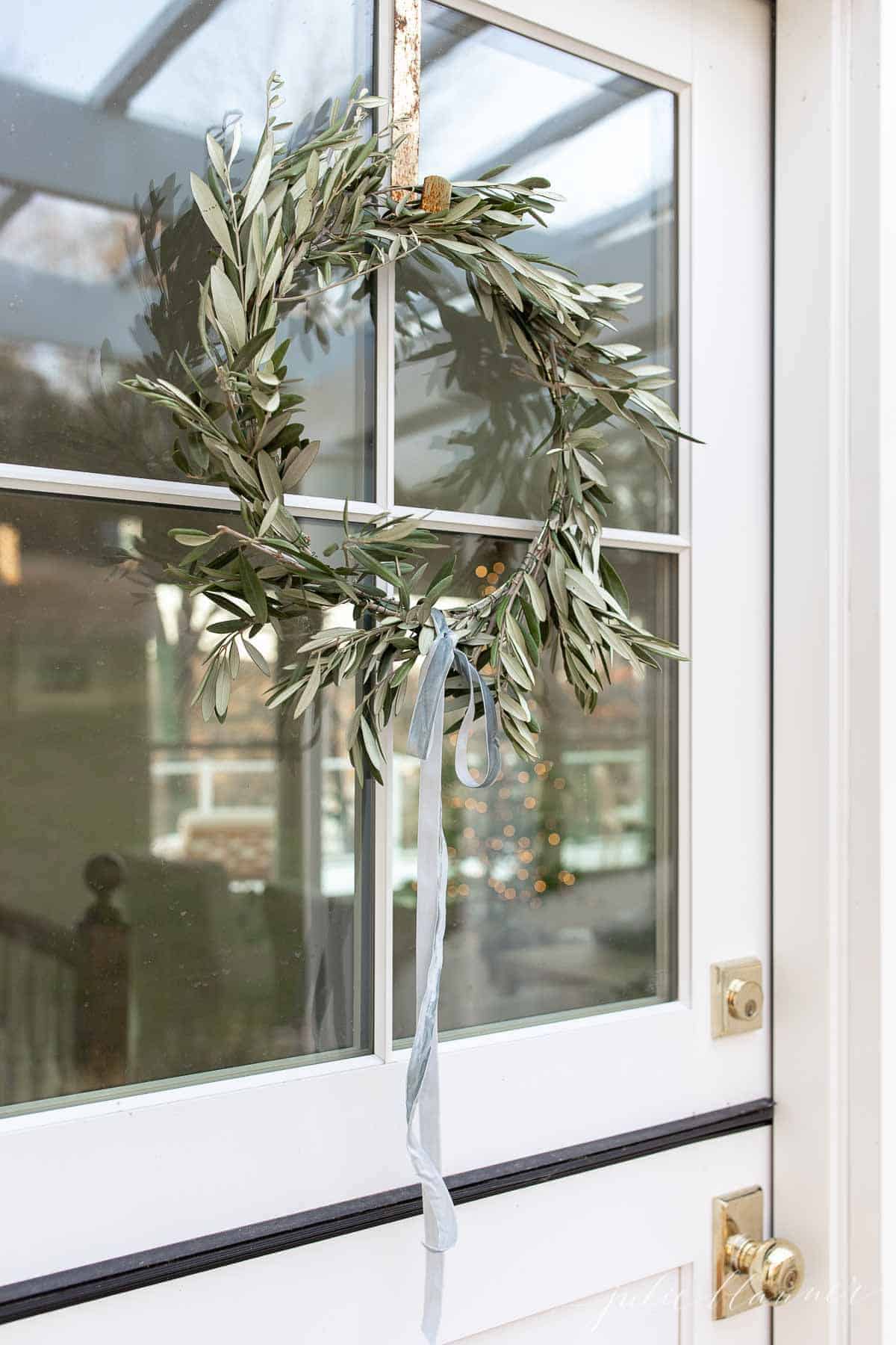 A dutch door with a DIY wreath hanging on the windows, looking into a living room decorated for Christmas.