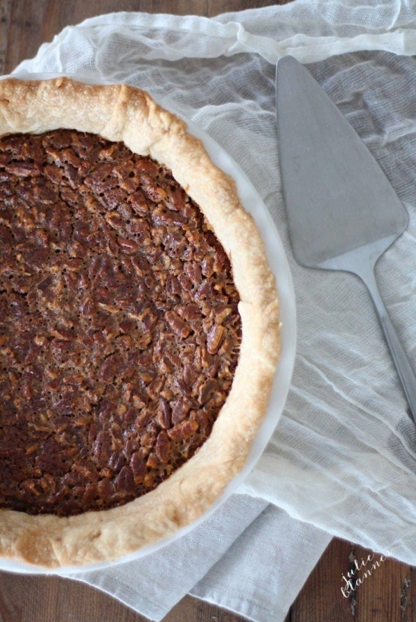 Caramel pecan pie in a white pie pan, a pie cutter to the side.