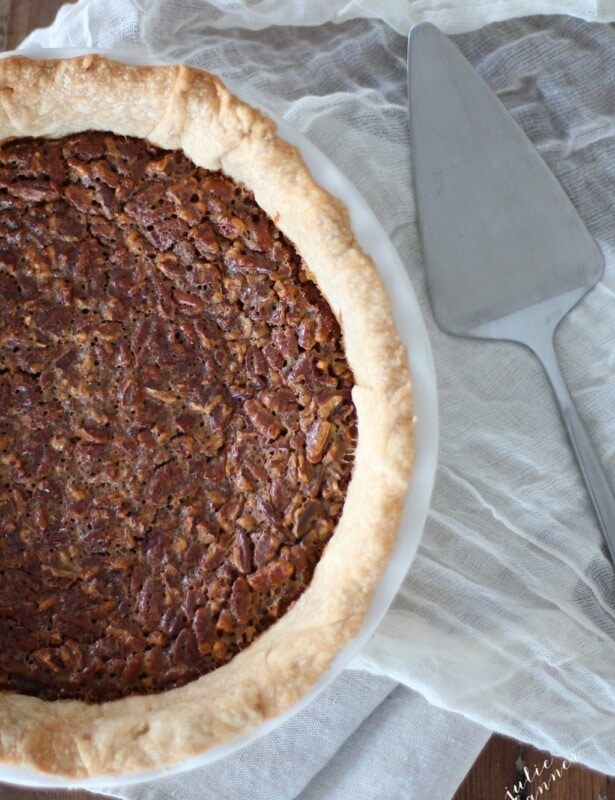 Caramel pecan pie in a white pie pan, a pie cutter to the side.