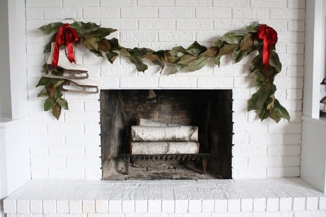 Garland with red ribbons and ice skates draped over a white fireplace.