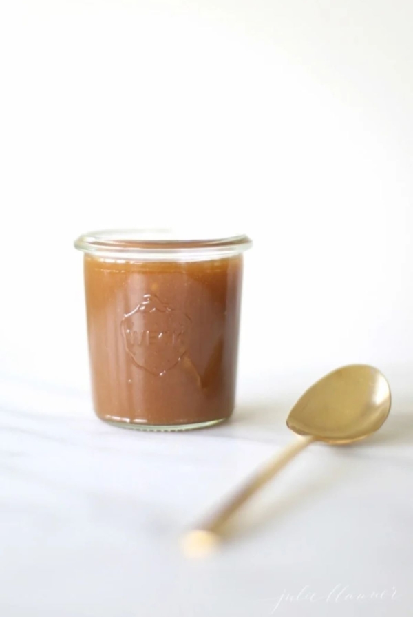 A small glass jar filled with salted caramel sauce, gold spoon to the side