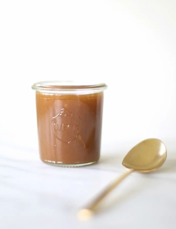 A small glass jar filled with salted caramel sauce, gold spoon to the side