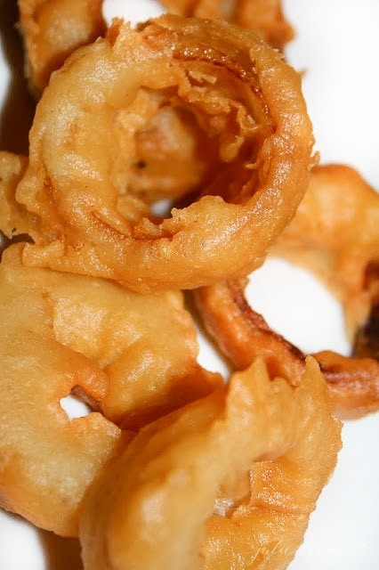 goldren brown homemade onion rings made with beer batter on a white plate
