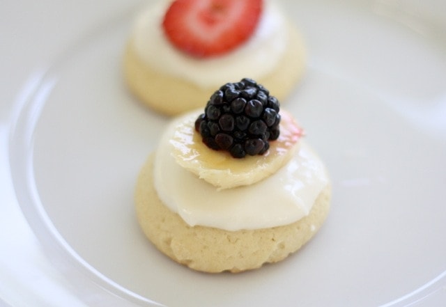 A mini fruit pizza topped with icing and a blackberry