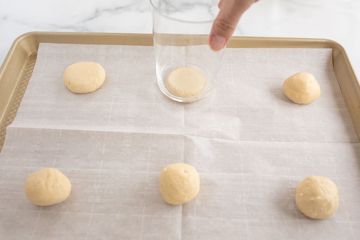 Sugar cookies being pressed on a gold baking sheet