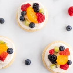 A white countertop with mini fruit pizza cookies and berries spread around