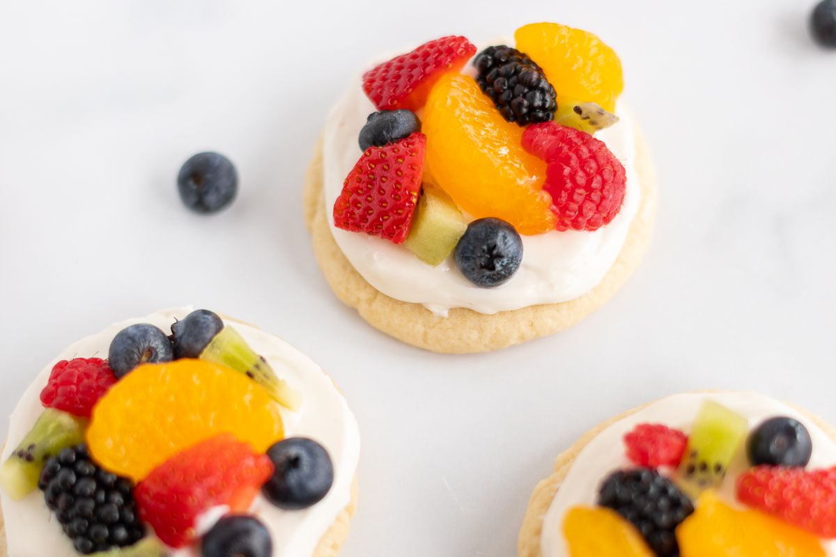 A white countertop with mini fruit pizza cookies and berries spread around