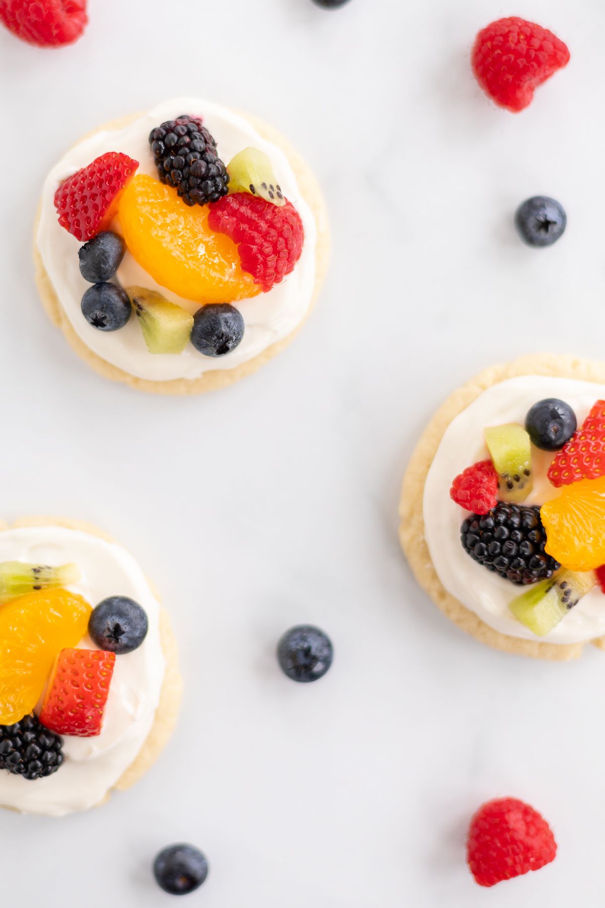 A white countertop with mini fruit pizza cookies and berries spread around