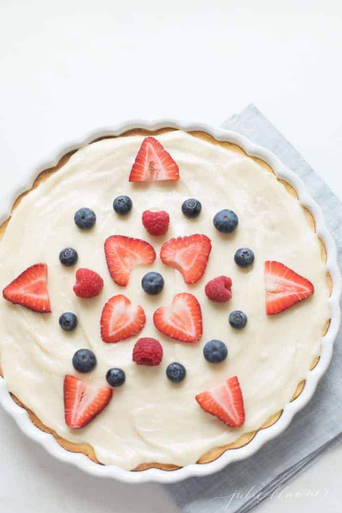 A fruit pizza decorated with fruit pizza icing and sliced berries.