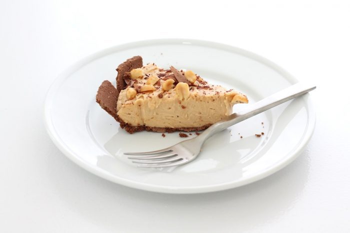 An easy No Bake Peanut Butter Cheesecake recipe tucked inside an Oreo or chocolate graham cracker crust. Creamy, crunchy, and decadently rich. slice of peanut butter and chocolate cheesecake on white plate with fork