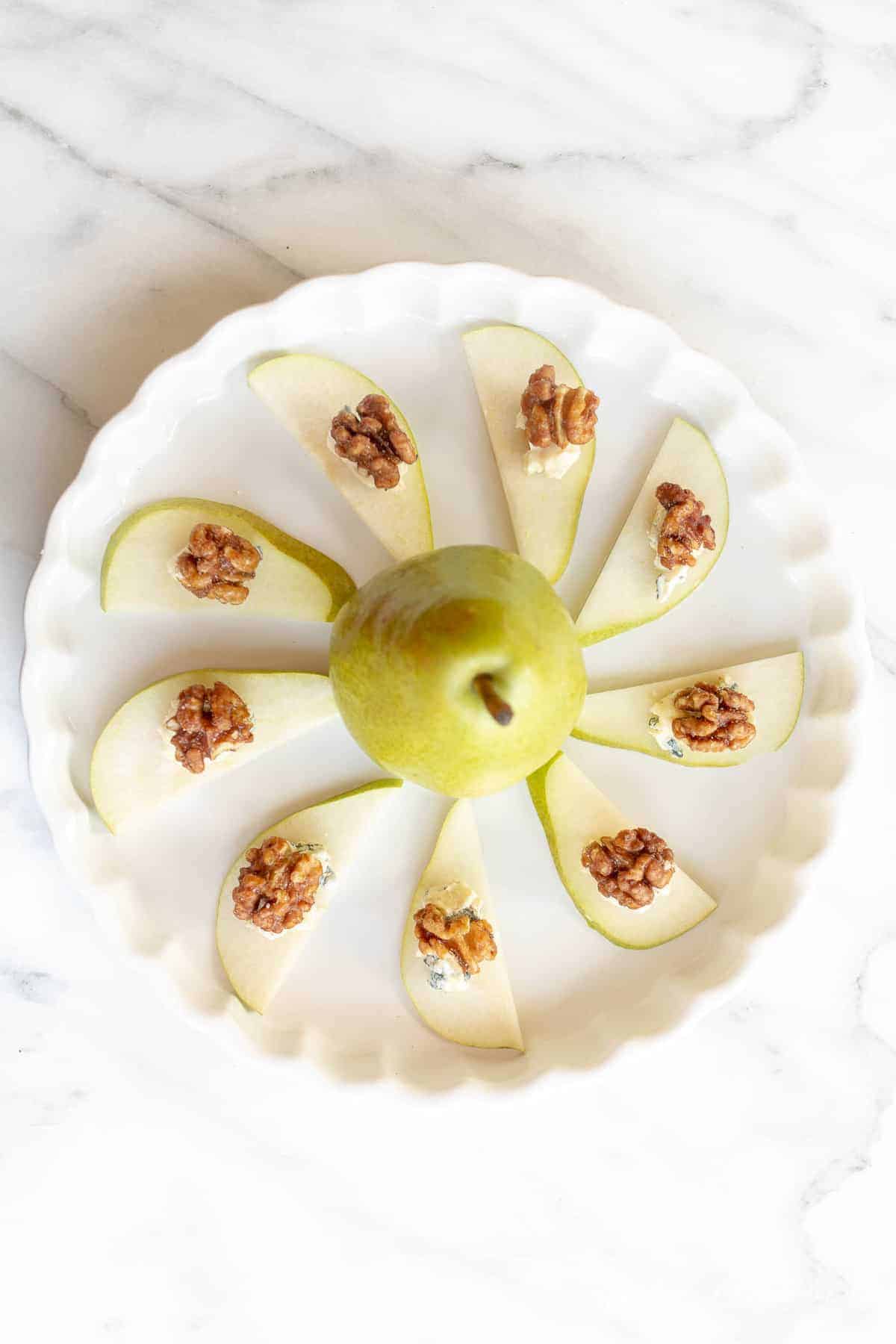 individual pear slices topped blue cheese and walnuts on a platter