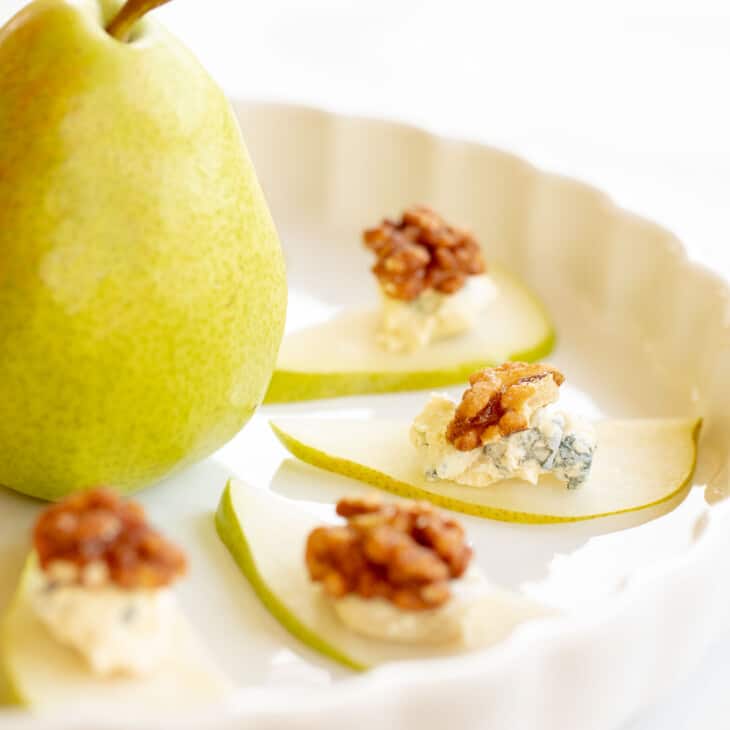 Thin pear slices topped with blue cheese and candied walnuts on a white platter with a pear in the middle.