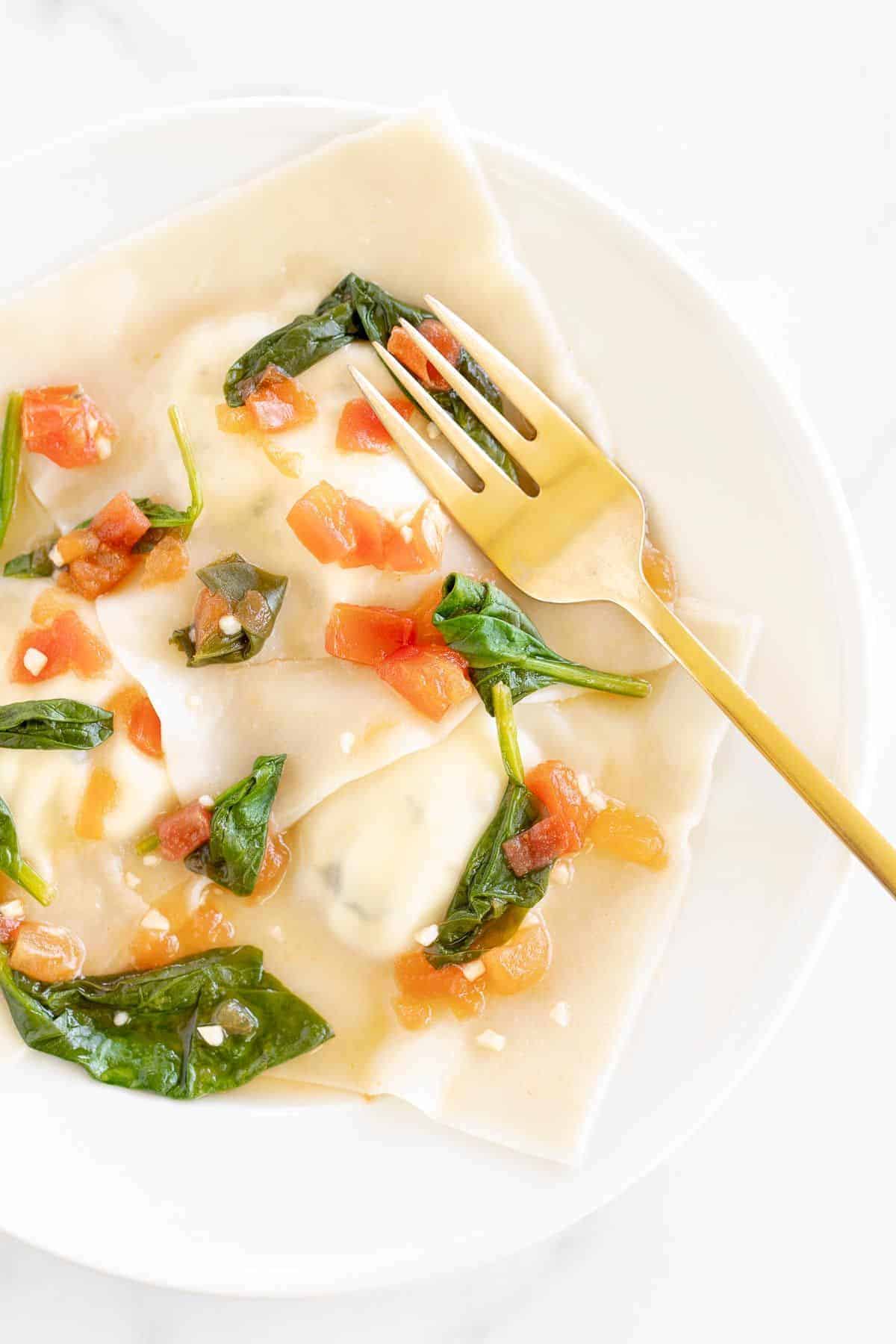A plate of goat cheese ravioli topped with a spinach and tomato based sauce.