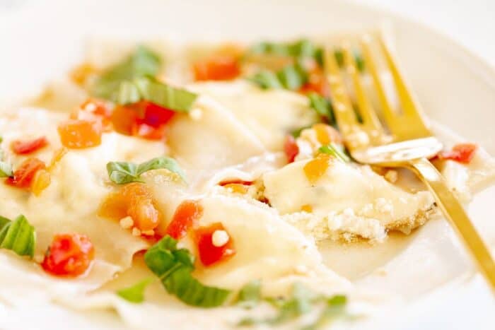 A white plate with goat cheese ravioli in a light tomato sauce, gold fork to the side.