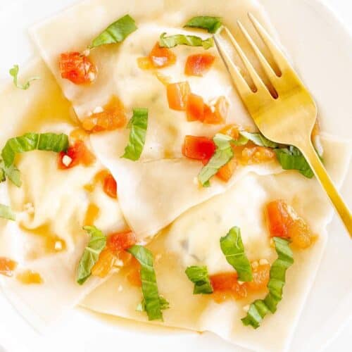 A white plate with goat cheese ravioli in a light tomato sauce, gold fork to the side.
