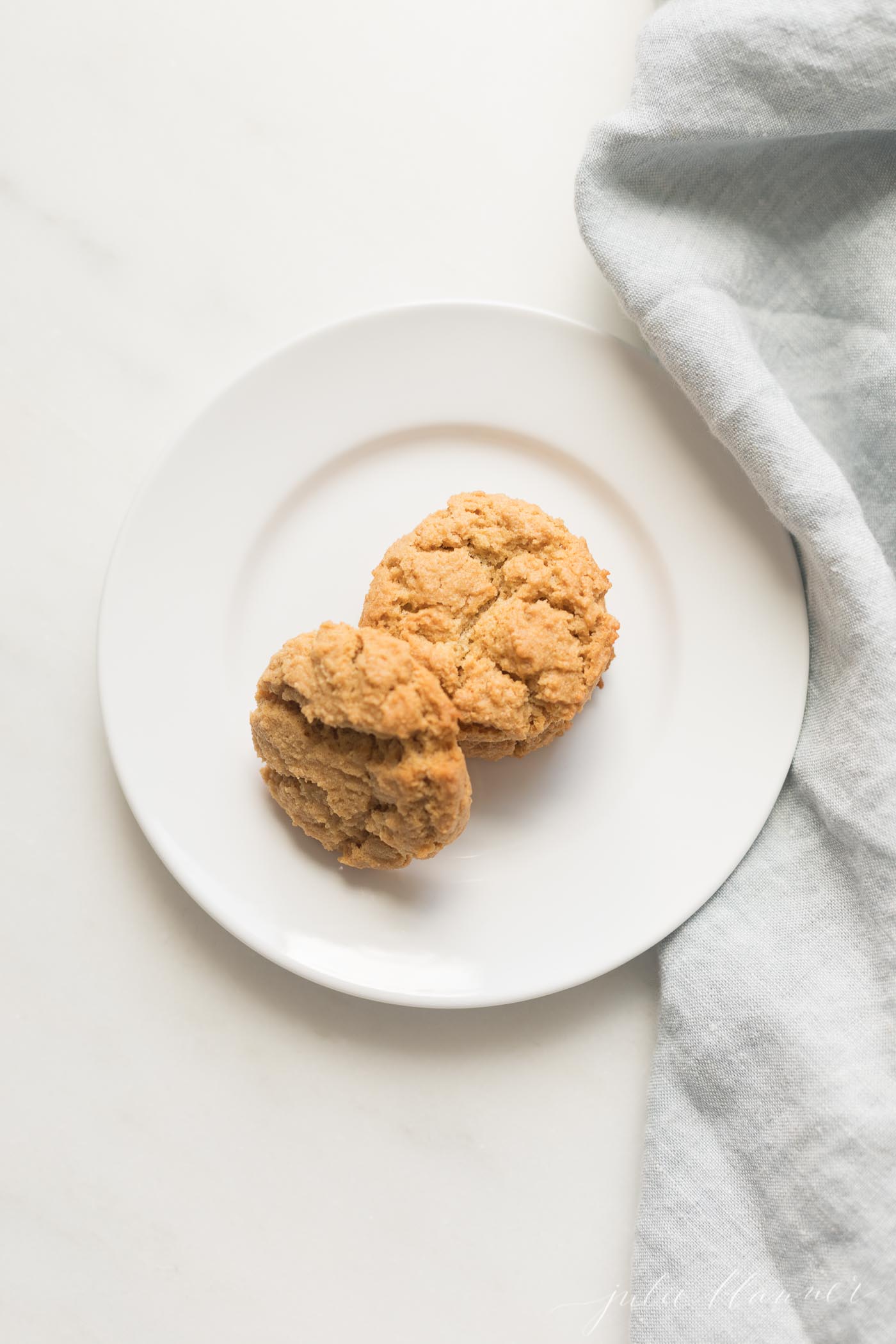 A white plate with flourless peanut butter cookies, blue linen kitchen towel to the side.