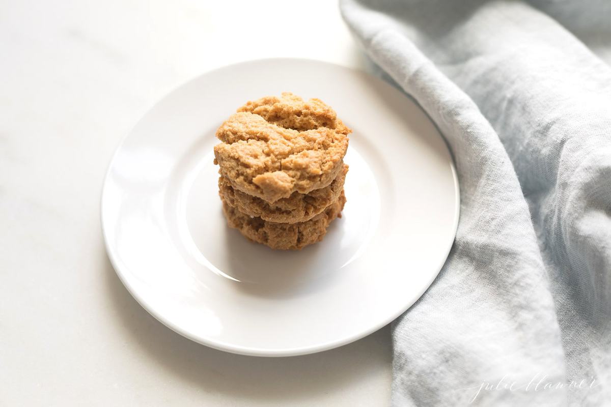 A white plate with a stack of gluten free peanut butter cookies, blue kitchen towel to the side.