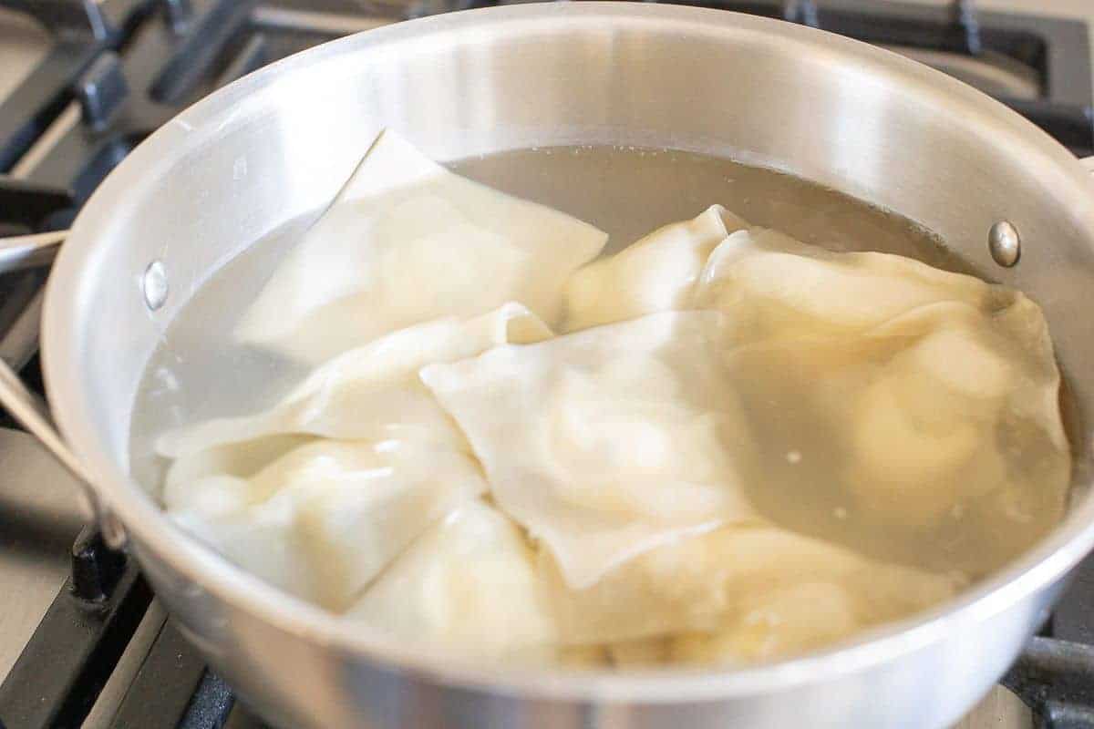 A silver pan full of water cooking goat cheese ravioli.