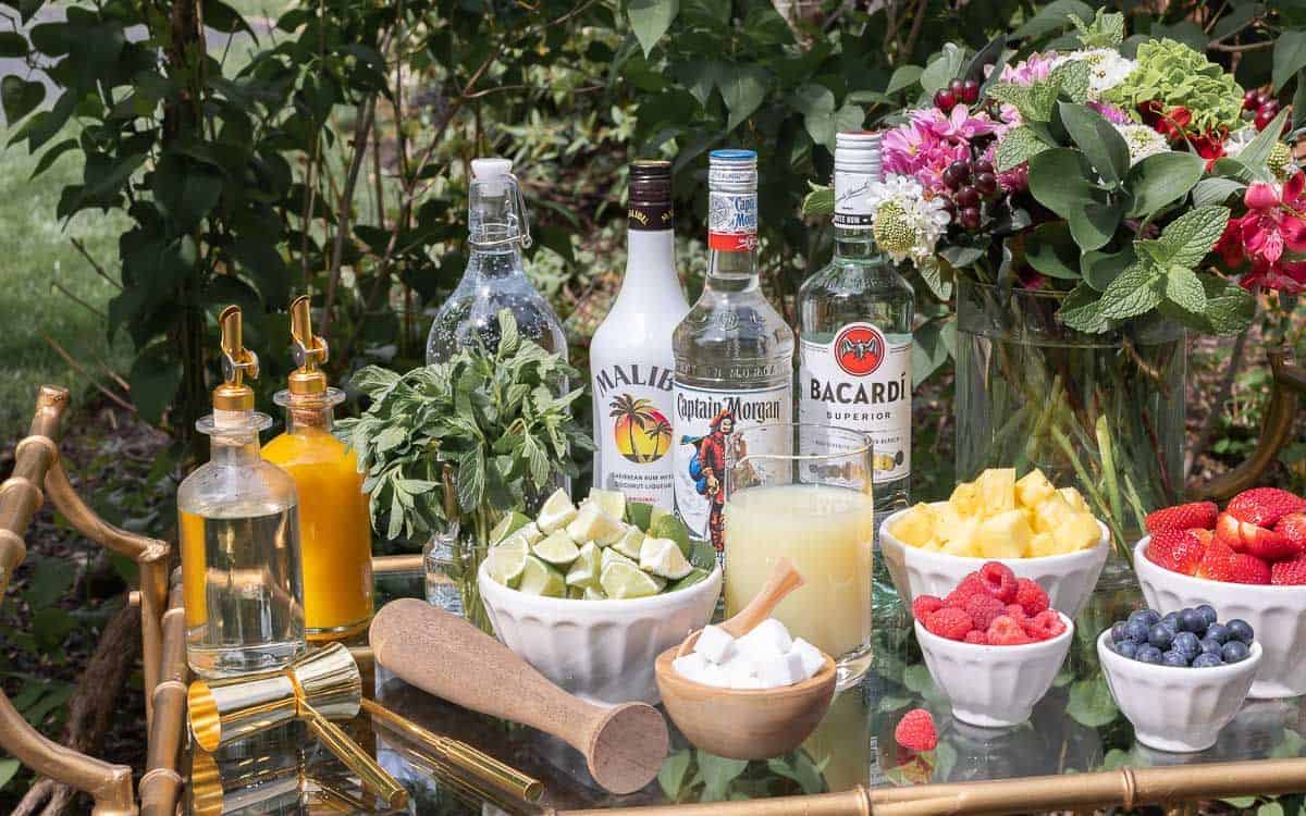 A glass and brass bar cart set up with a mojito bar outdoors.