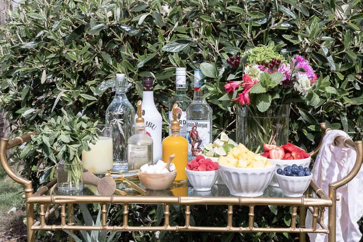 A glass and brass bar cart set up with a mojito bar outdoors.