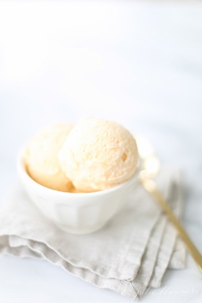 No churn homemade peach ice cream recipe in a white bowl placed on top of a linen kitchen towel.