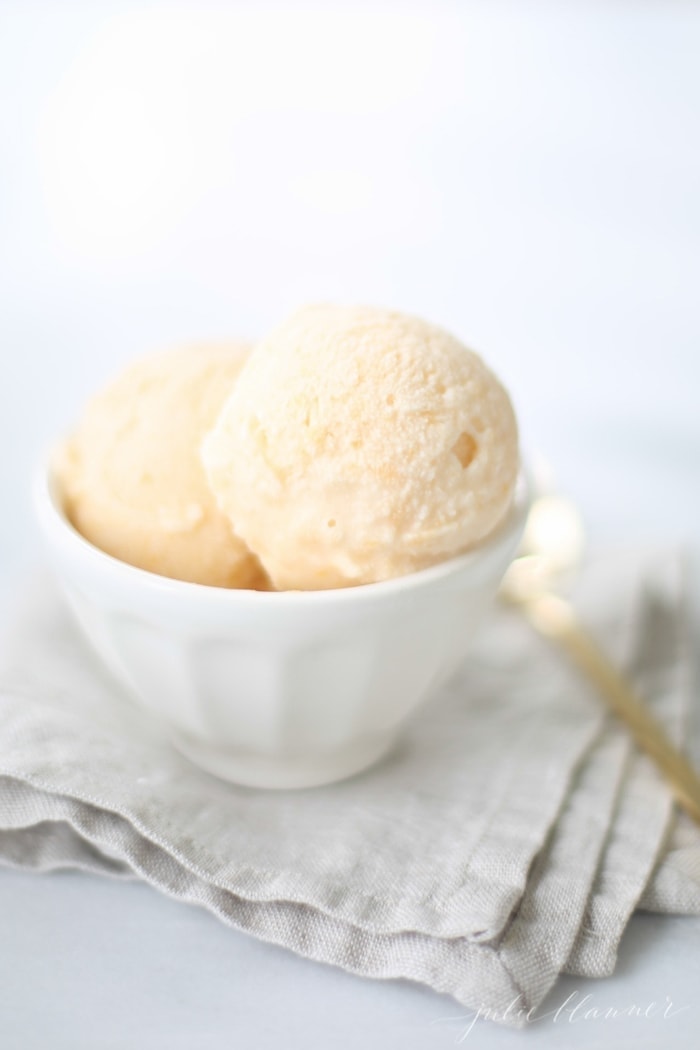 No churn homemade peach ice cream recipe in a white bowl placed on top of a linen kitchen towel.