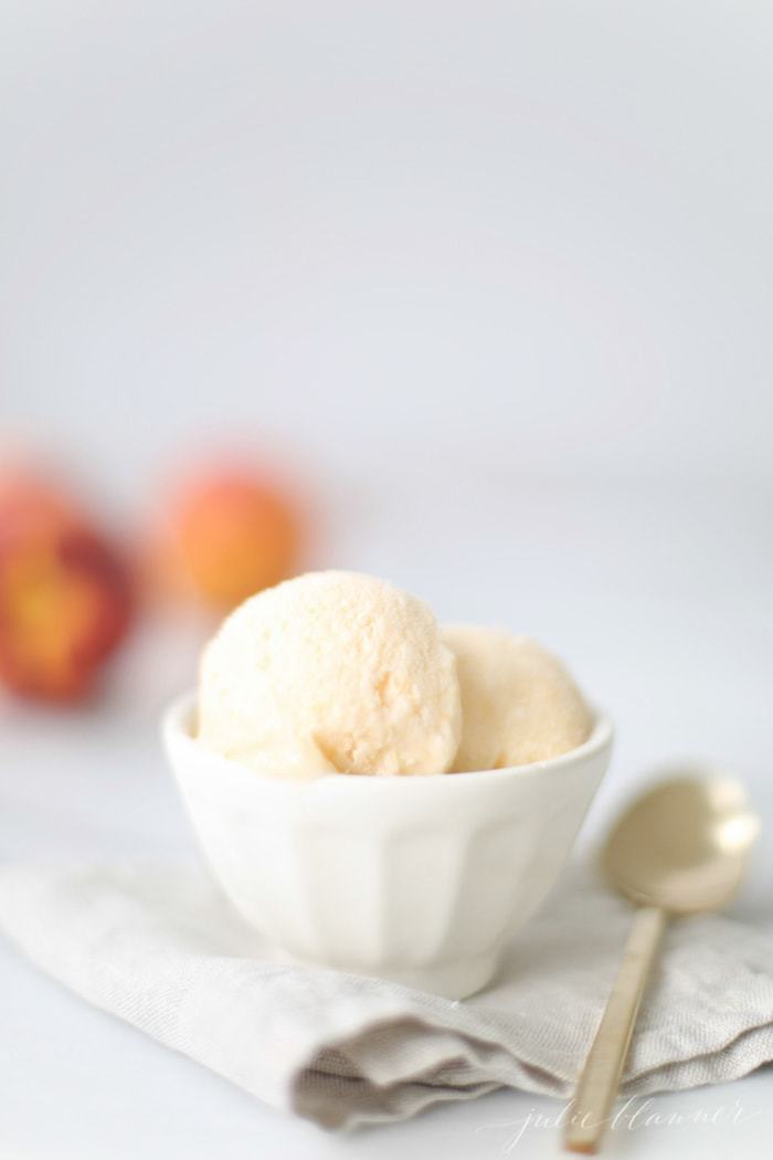 No churn homemade peach ice cream recipe in a white bowl placed on top of a linen kitchen towel.